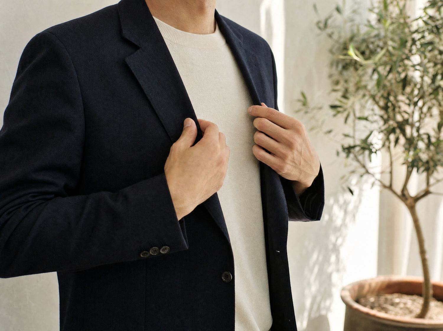 Hands adjusting the lapel of a navy blazer over a cream knit sweater