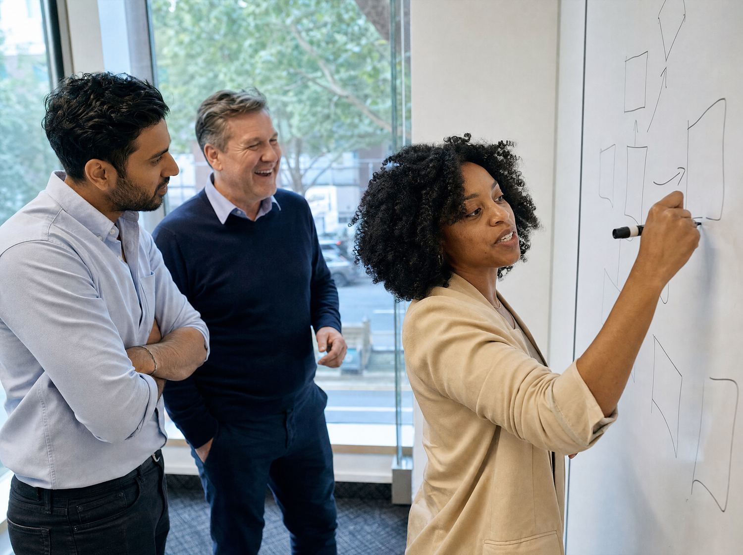 Three colleagues of different ages talking through a sketch at a whiteboard